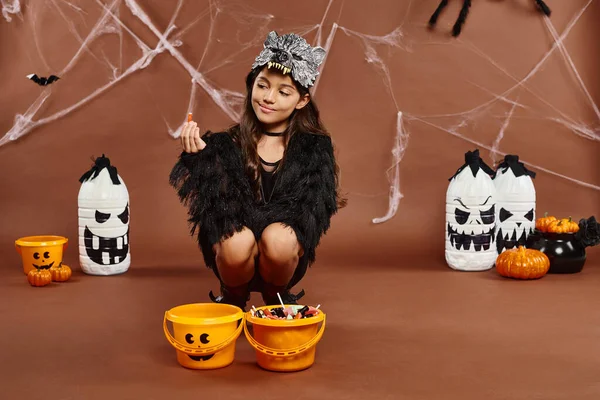 Дівчина присідає біля відер цукерок і тримає цукерки, концепція Хеллоуїна — стокове фото