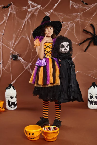 Preteen girl in witch hat with spooky toy and touching her cheek and looks away, Halloween — Stock Photo