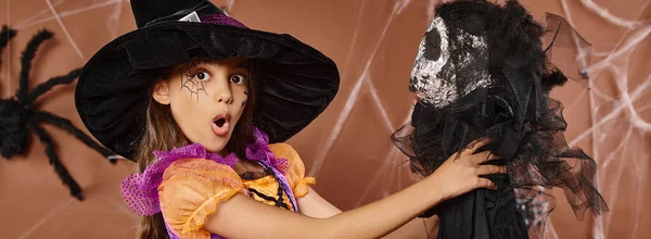 Close up surprised kid in witch hat and spiderweb makeup holds scary toy, Halloween, banner — Stock Photo