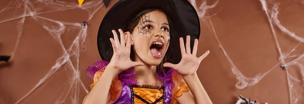 Chica emocional en sombrero de bruja y disfraz de Halloween gritando sobre fondo marrón, bandera - foto de stock