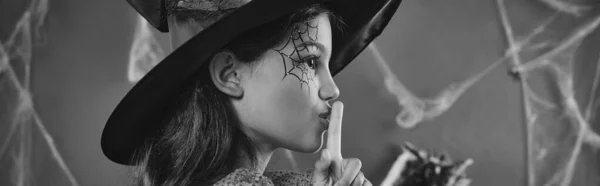 Bonito menina no Halloween bruxa traje e apontou chapéu mostrando shh preto e branco banner — Fotografia de Stock