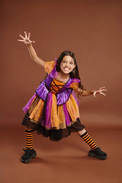 Fille effrayante en costume de sorcière Halloween grogner et gesticuler sur fond brun, pleine longueur — Photo de stock