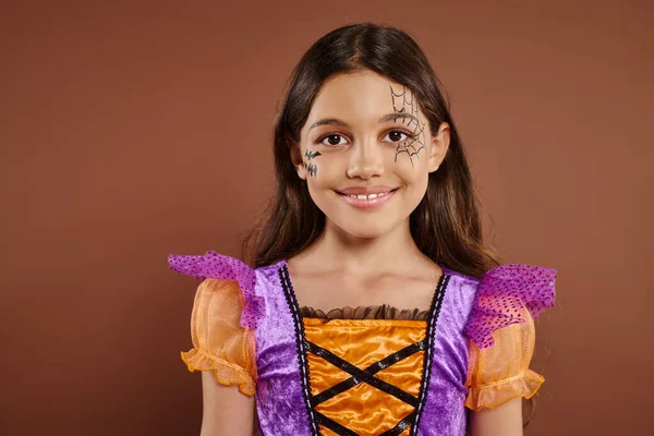 Очаровательная девушка в костюме Хэллоуина и паутины макияж улыбаясь на коричневом фоне, трюк или удовольствие — стоковое фото