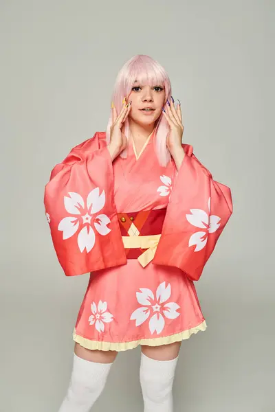 Jovem mulher loira com manicure colorido vestindo quimono rosa e olhando para a câmera no cinza — Fotografia de Stock