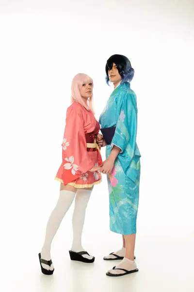 Comprimento total de cosplayers jovens em quimonos coloridos de mãos dadas e olhando para a câmera no branco — Fotografia de Stock