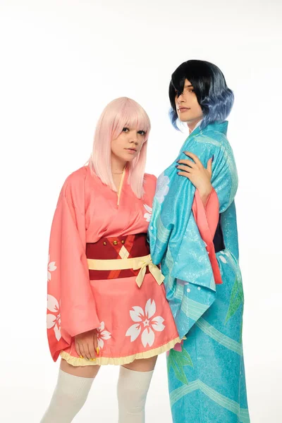 Donna bionda in stile anime che abbraccia il braccio dell'uomo in kimono e parrucca su bianco, concetto di sottocultura cosplay — Foto stock