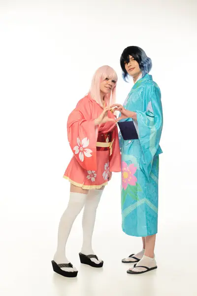 Счастливые молодые косплееры в цветных кимоно, показывающие сердечный знак руками в белом, аниме стиле — стоковое фото