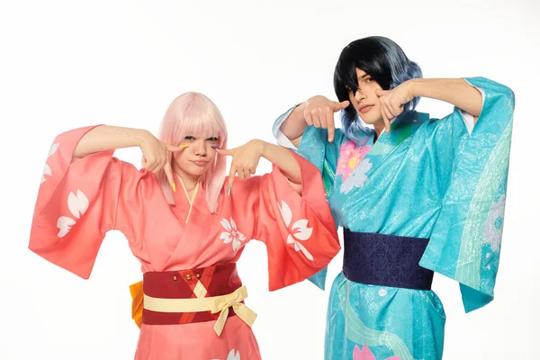 Jeunes cosplayers en kimonos lumineux pointant vers le bas avec les doigts sur blanc, concept de style anime — Photo de stock