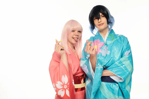 Femme blonde en kimono sortant de la langue et montrant des mini-coeurs signes avec anime homme sur blanc — Photo de stock