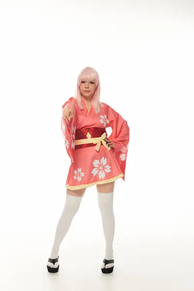 Full length of woman in blonde wig and pink kimono pointing at camera on white, cosplay culture — Stock Photo