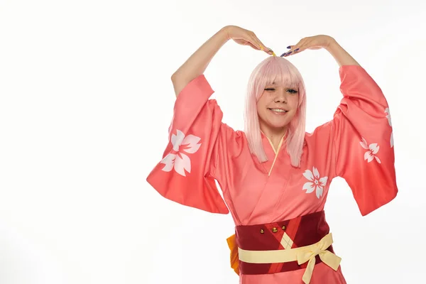 Flerte anime mulher em kimono rosa de pé em pose expressiva e piscando no fundo branco — Fotografia de Stock