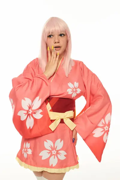 Шокована жінка в аніме-стилі рожева з рукою на хіпі, торкаючись обличчя на білому, косплей персонаж — стокове фото
