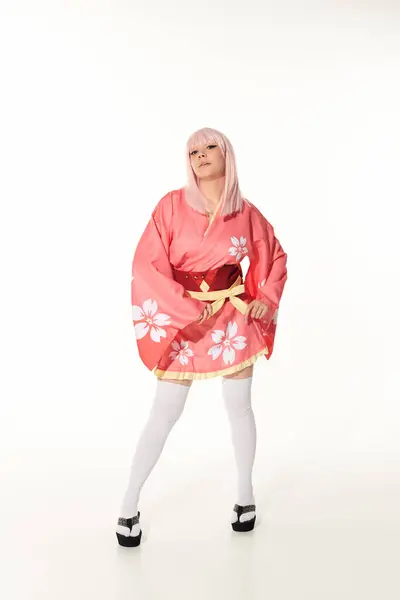 Expresiva mujer anime en kimono rosa y peluca rubia mirando a la cámara en blanco, longitud completa - foto de stock