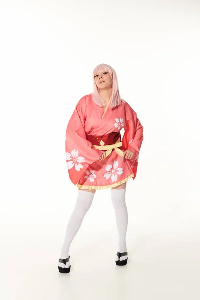 Expressive anime woman in pink kimono and blonde wig looking at camera on white, full length — Stock Photo