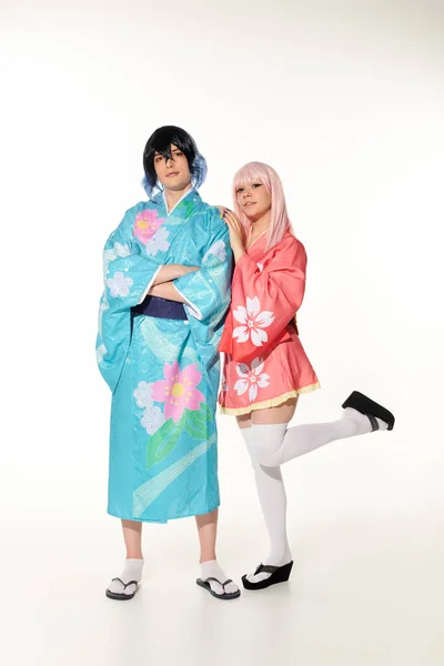 Mujer apoyada en novio en colorido kimono y peluca de pie con los brazos cruzados en blanco, cosplay - foto de stock