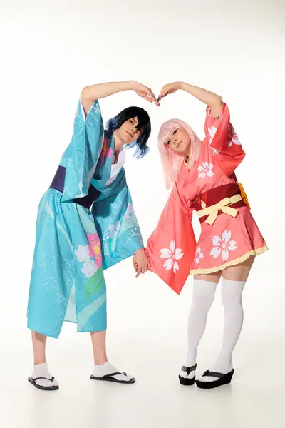 Romantic cosplayers in wigs and bright kimonos showing great heart sign with hands on white — Stock Photo