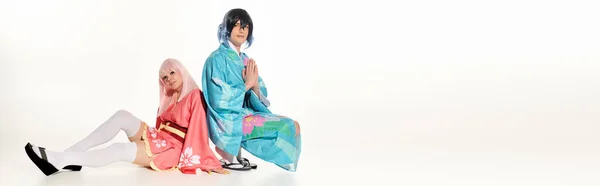 Man in kimono with praying hands near anime woman in blonde wig sitting on white, horizontal banner — Stock Photo