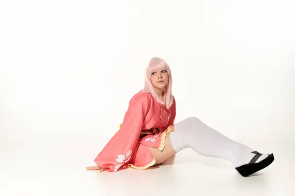 Mulher sonhadora em quimono rosa e peruca loira sentado e olhando para longe em branco, personagem de anime — Fotografia de Stock