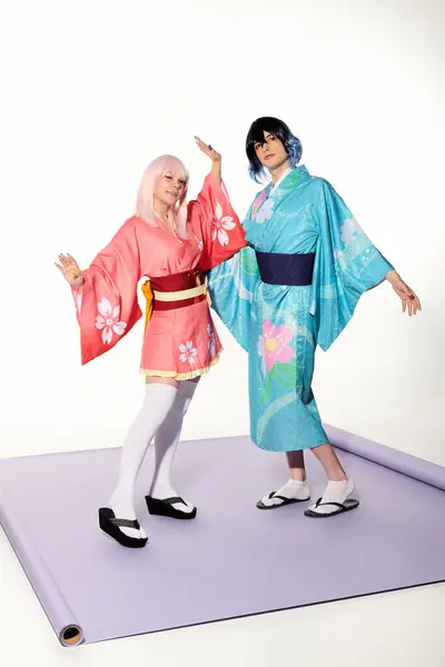 Jovens cosplayers expressivos em quimonos coloridos e perucas posando no tapete roxo no estúdio branco — Fotografia de Stock