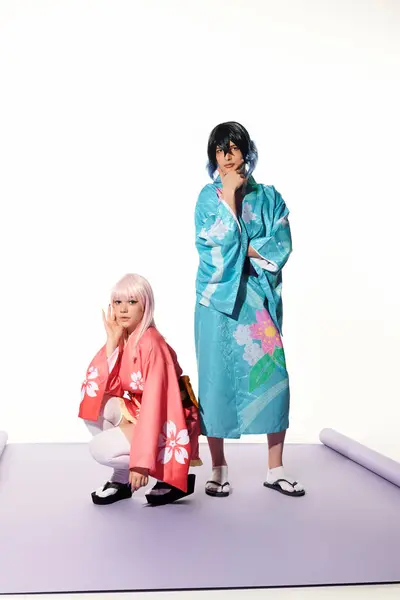Donna anime bionda seduta su fianchi vicino all'uomo in kimono e parrucca sul tappeto viola in studio bianco — Foto stock