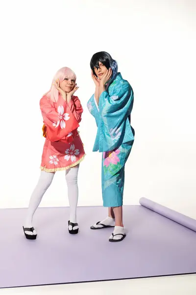 Verspieltes Paar Cosplayer in lebendigem Outfit, die Gesichter auf lila Teppich und weißem Hintergrund berühren — Stockfoto