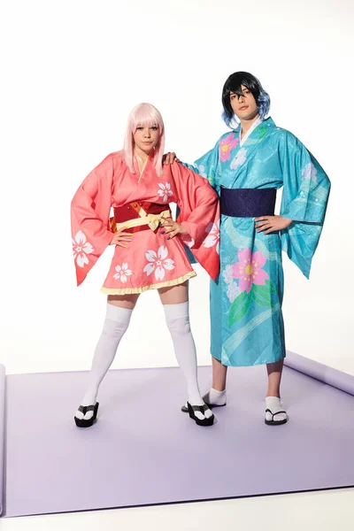 Selbstbewusstes, ausdrucksstarkes Paar in farbenfrohen Kimonos und Flügeln, das mit den Händen an den Hüften posiert, Cosplay-Trend — Stockfoto