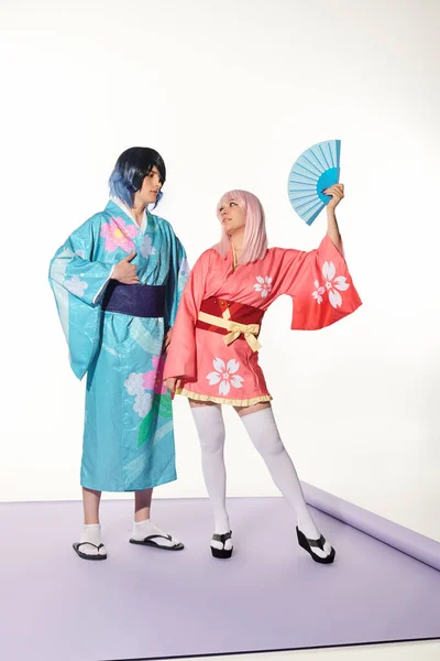 Mulher loira com peruca perto do homem em quimono colorido no tapete roxo no branco, cultura cosplay — Fotografia de Stock