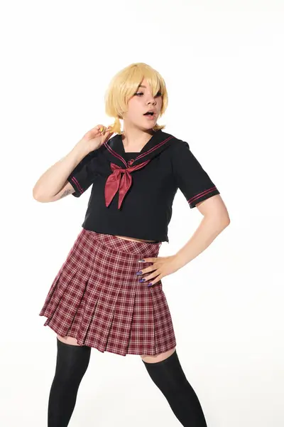 Surprised anime woman in school uniform and yellow blonde wig standing with hand on hip on white — Stock Photo
