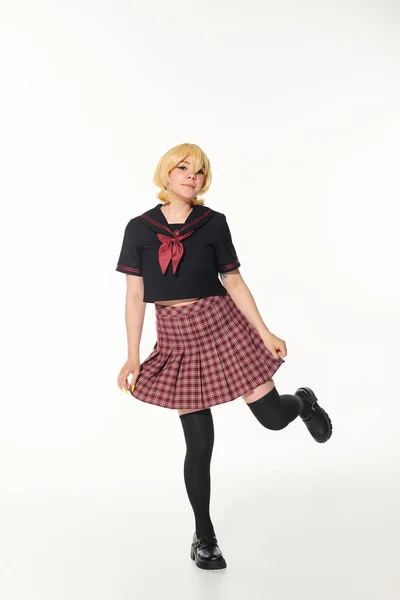 Jolly young woman in school uniform posing on one leg on white, youthful cosplay subculture — Stock Photo