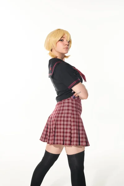 Confiante anime estilo mulher em amarelo loira peruca e uniforme escolar com braços dobrados em branco — Fotografia de Stock