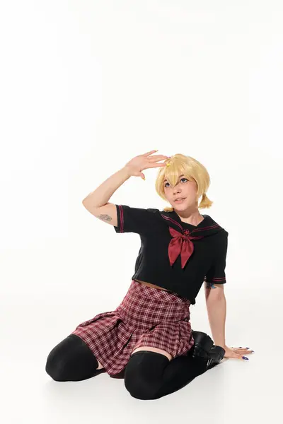 Tattooed blonde woman in stylish school uniform sitting and waving hand on white, anime style — Stock Photo