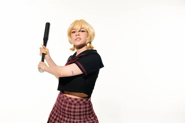 Mujer irritada en uniforme escolar y peluca de pie con bate de béisbol en blanco, personaje cosplay - foto de stock