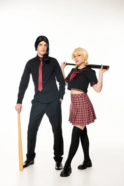 Full length of young cosplayers in dark school uniform and wigs with baseball bats on white — Stock Photo