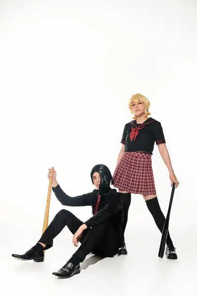 Couple confiant de style anime en uniforme scolaire et perruques avec posant avec des chauves-souris de baseball sur blanc — Photo de stock