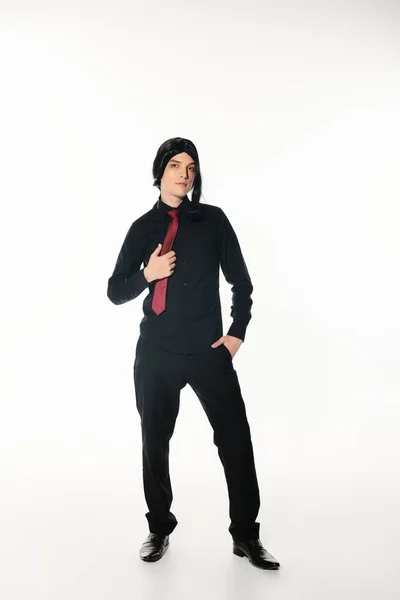 Joven cosplayer en ropa negra y corbata roja de pie con la mano en el bolsillo en blanco, cultura juvenil - foto de stock
