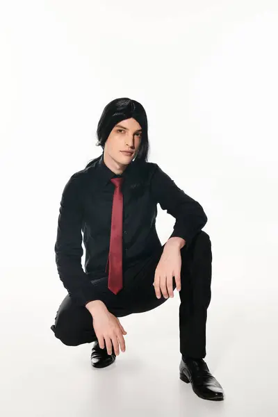 Fashionable man in black clothes and  wig with red tie sitting on haunches on white, cosplay trend — Stock Photo