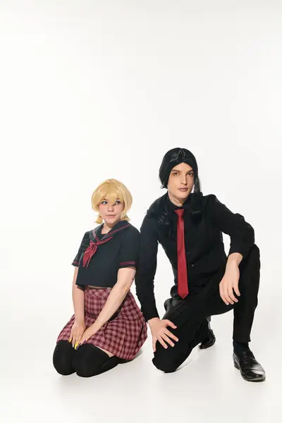 Anime-Stil Studenten in blonden und schwarzen Perücken und Uniform sitzen und schauen in die Kamera auf weiß — Stockfoto