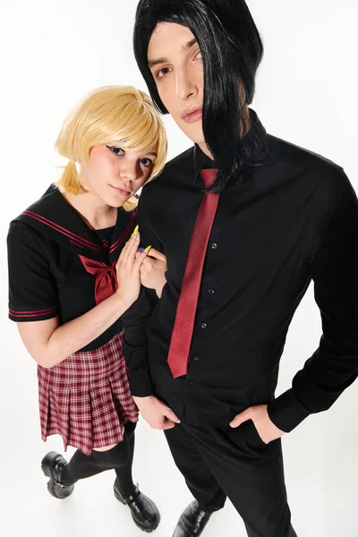 Visão ampla ângulo de casal estilo cosplay em perucas e estudantes escuros uniforme olhando para a câmera no branco — Fotografia de Stock