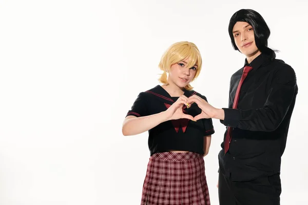 Cosplay couple in black and blonde wigs showing heart sign with hands looking at camera on white — Stock Photo