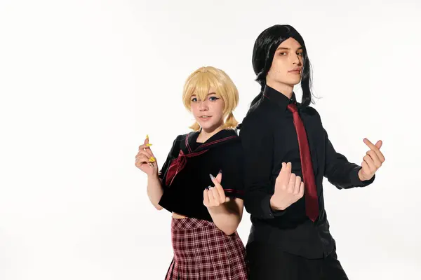 Jóvenes estudiantes de estilo anime en uniforme oscuro y pelucas que muestran mini corazones con los dedos en blanco - foto de stock