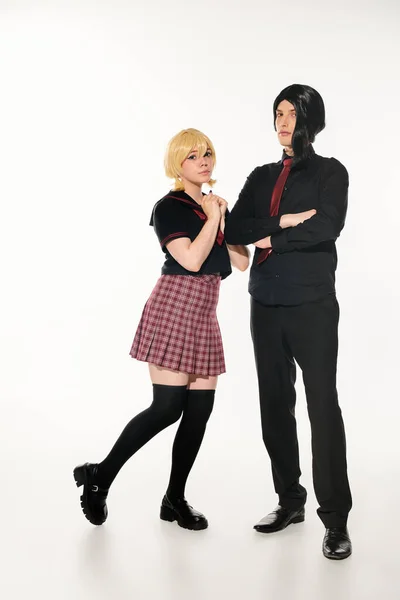 Femme en perruque blonde près de l'homme confiant en vêtements noirs avec les bras croisés sur noir, étudiants cosplay — Photo de stock