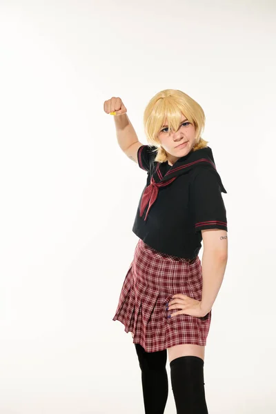 Angry woman in school uniform and yellow blonde wig showing fist on white, cosplay character — Stock Photo