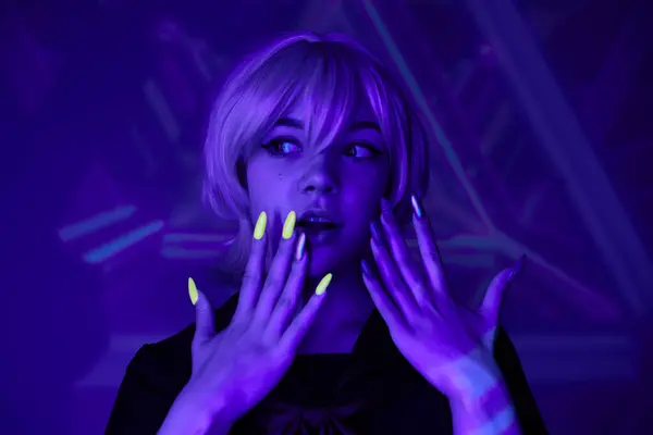 Изумленная блондинка с флуоресцентным маникюром в синем неоновом свете на абстрактном фоне, в стиле аниме — стоковое фото