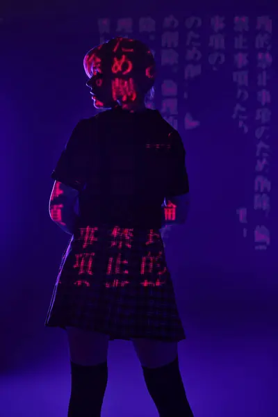 Vista posteriore della donna anime in uniforme scolastica in geroglifici proiezione su luce blu al neon, sottocultura — Foto stock