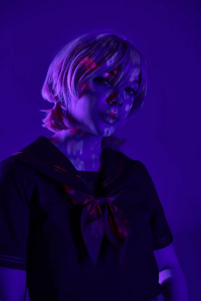 Porträt einer jungen Frau mit blonder Perücke, die in blauem Neonlicht in die Kamera blickt, Cosplay-Kulturkonzept — Stockfoto