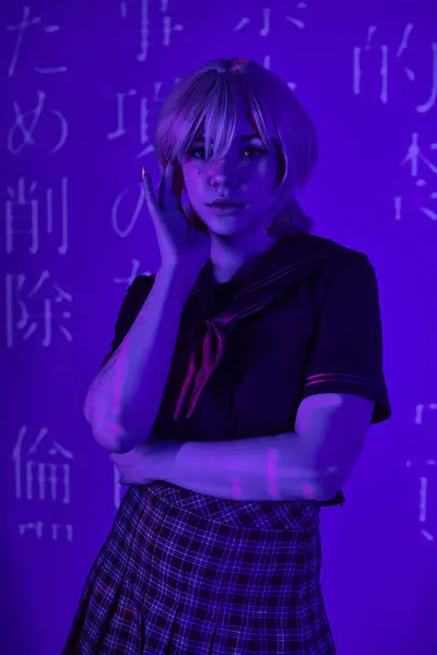 Donna in parrucca bionda e uniforme scolastica in luce blu al neon con geroglifici proiezione, tendenza anime — Foto stock