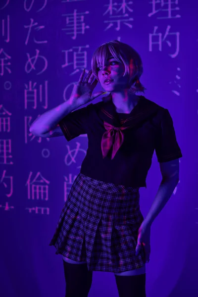 Молодая женщина в школьной форме смотрит в голубой неоновый свет с иероглифами проекции, косплей — стоковое фото