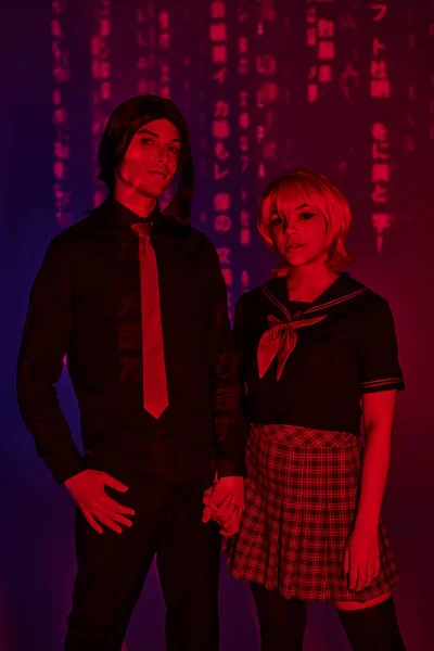 Anime style studenti in uniforme tenendosi per mano in luce rossa al neon su sfondo viola astratto — Foto stock