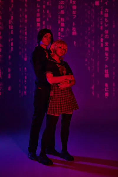 Stilvoller Mann umarmt Frau im Anime-Stil in Studentenuniform in rotem Neonlicht auf lila Hintergrund — Stockfoto