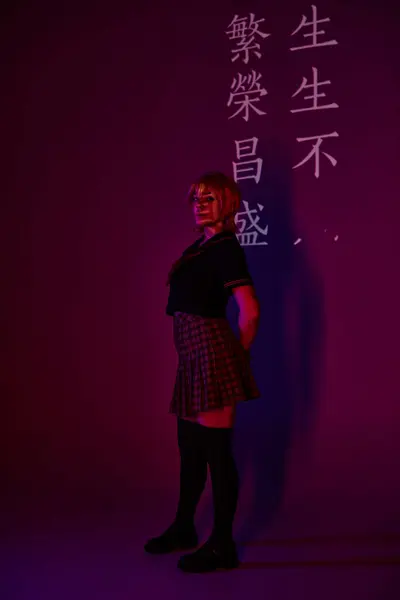 Жінка в шкільній формі в неоновому світлі на фіолетовому фоні з проекцією ієрогліфів, стиль аніме — стокове фото